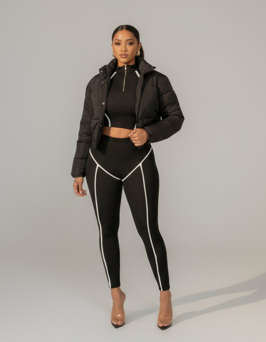 A person wearing a black lightweight puffer jacket with white accent lines on the side, paired with black leggings.