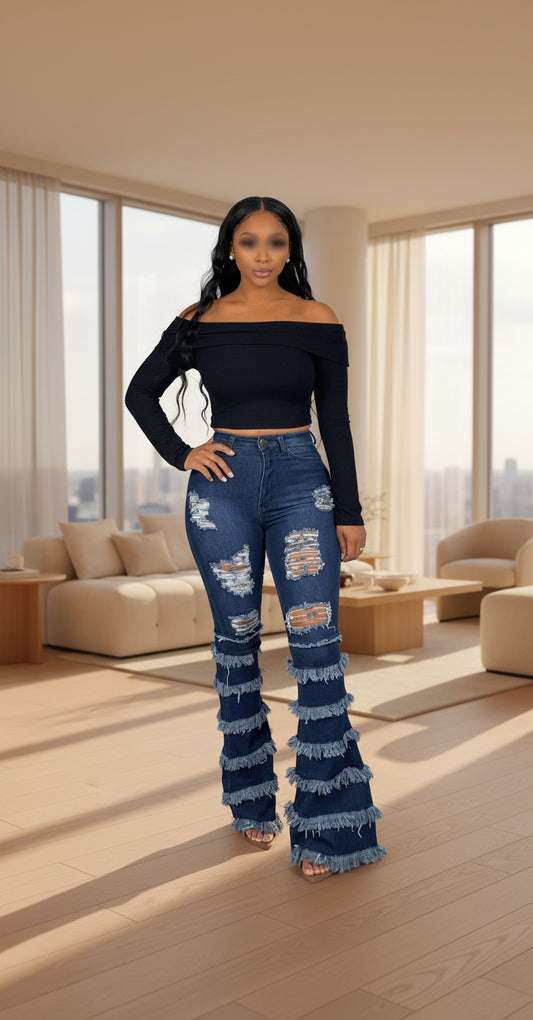 Woman wearing a black off-shoulder top and distressed blue jeans on a gray background